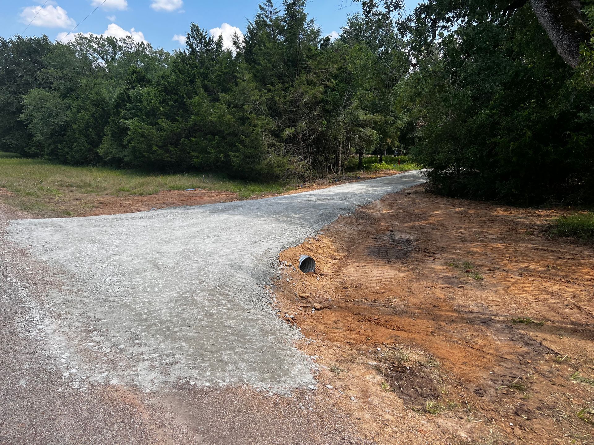 A gravel road with a culvert pipe leading into a wooded area.