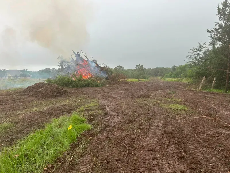 Burning brush pile with smoke in a muddy field on an overcast day.