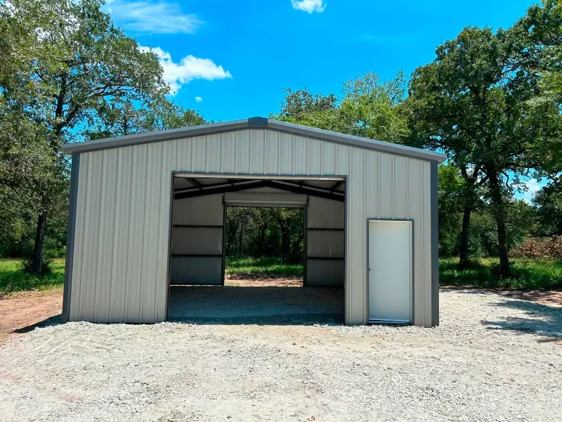 A large metal garage with a door open and trees in the background.