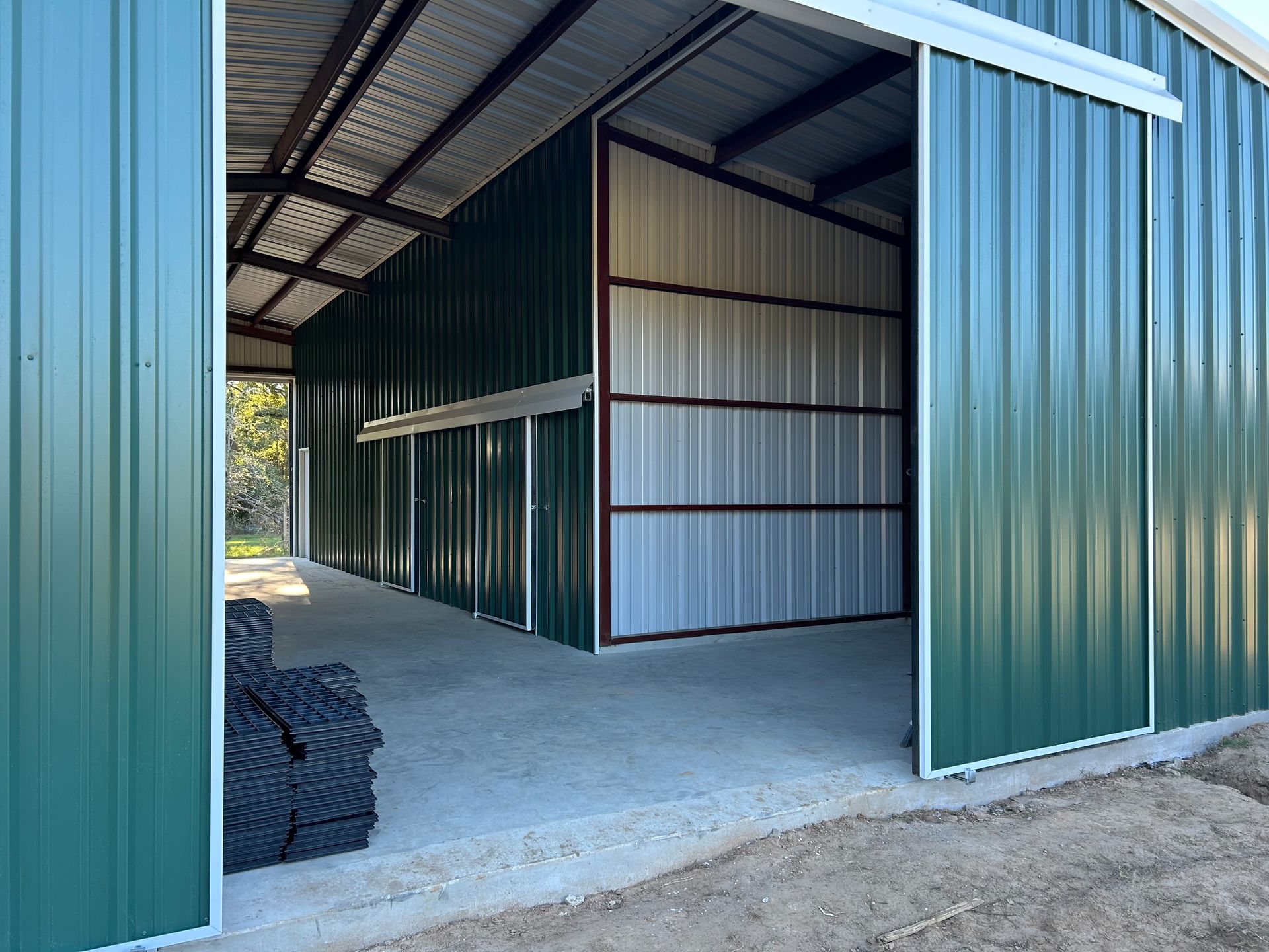Green metal storage building with open sliding doors and concrete floor.