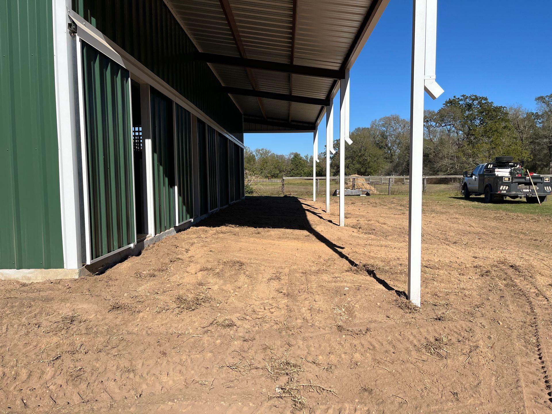 Green and white building with a covered walkway and dirt ground under a clear blue sky.