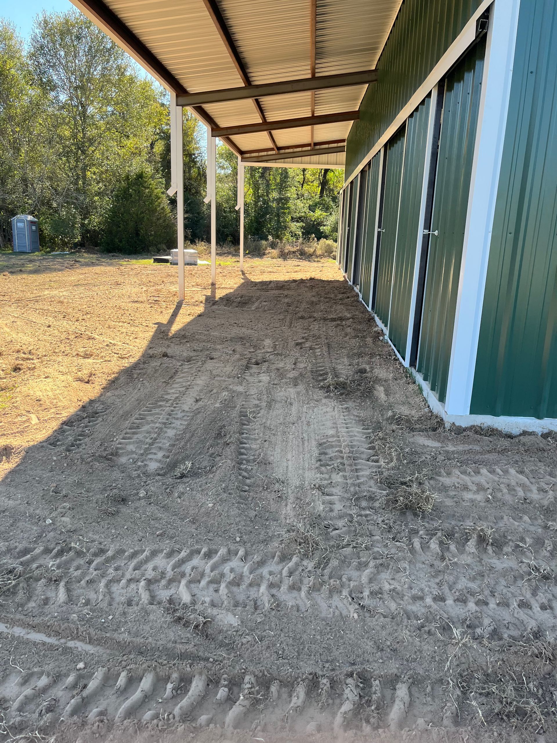 A gravel path under a metal awning next to a green metal building with white trim.