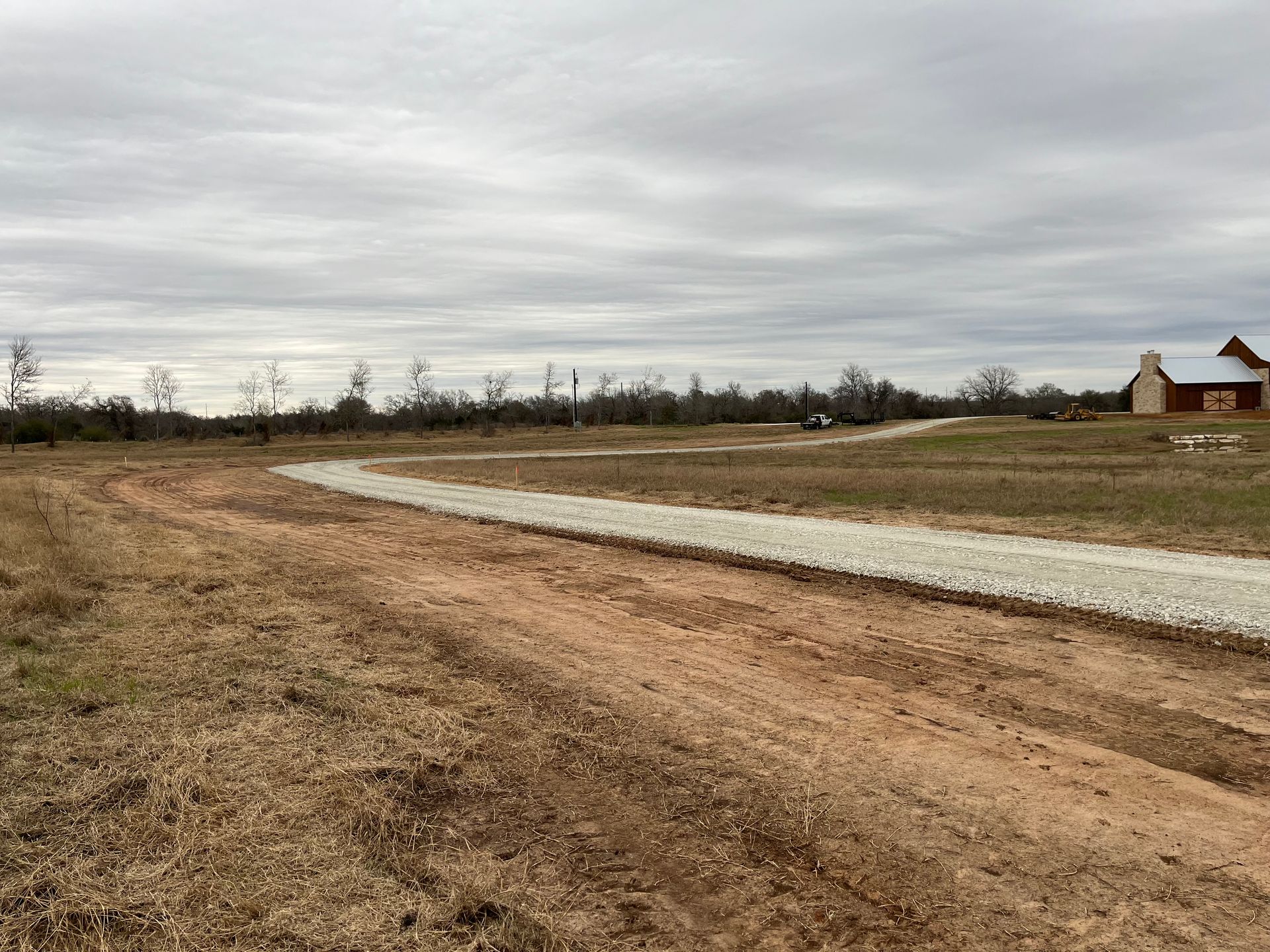 A dirt road going through a field with a house in the background.