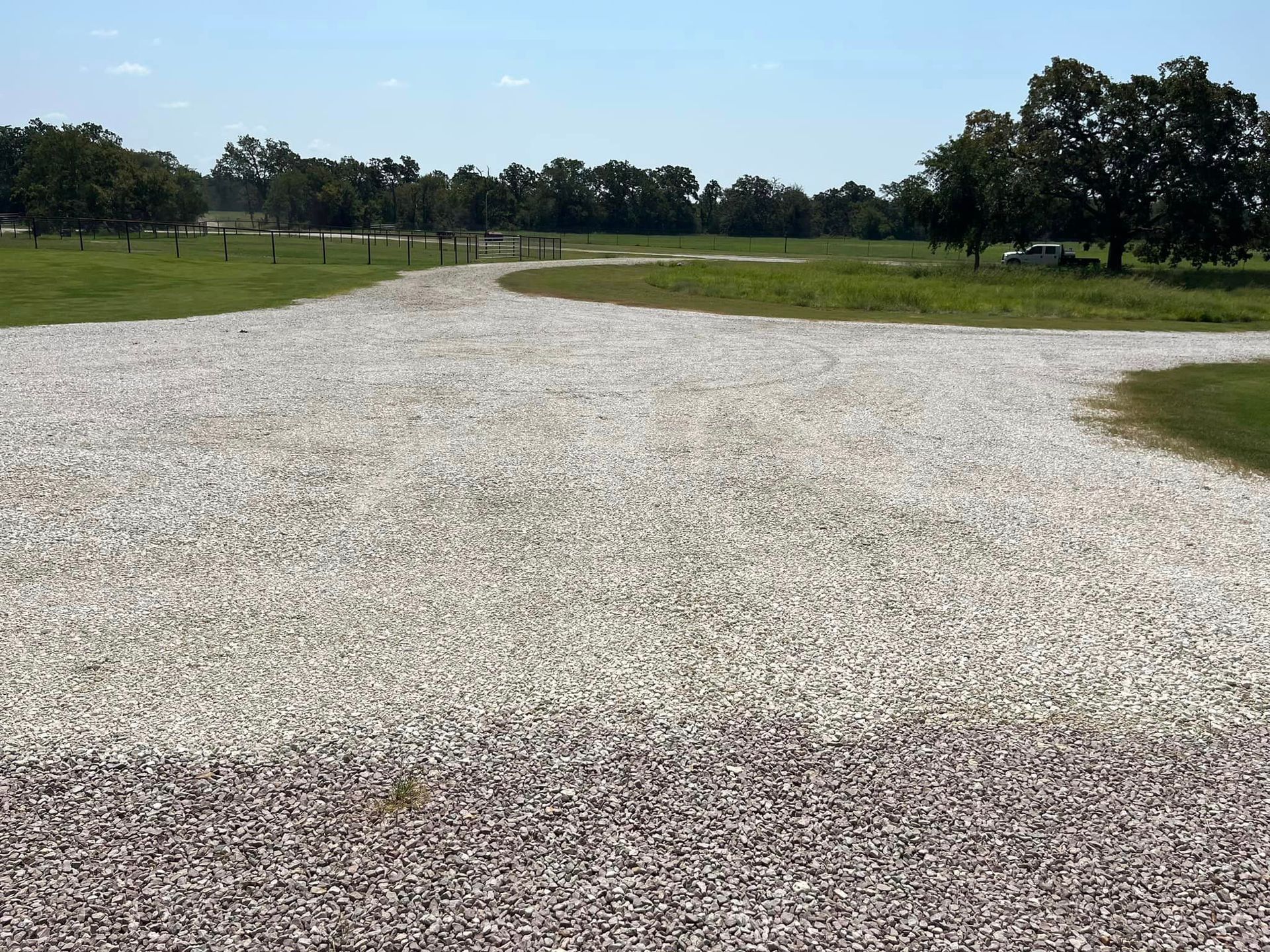 Gravel driveway forks into two paths, leading towards green fields and trees under a blue sky.