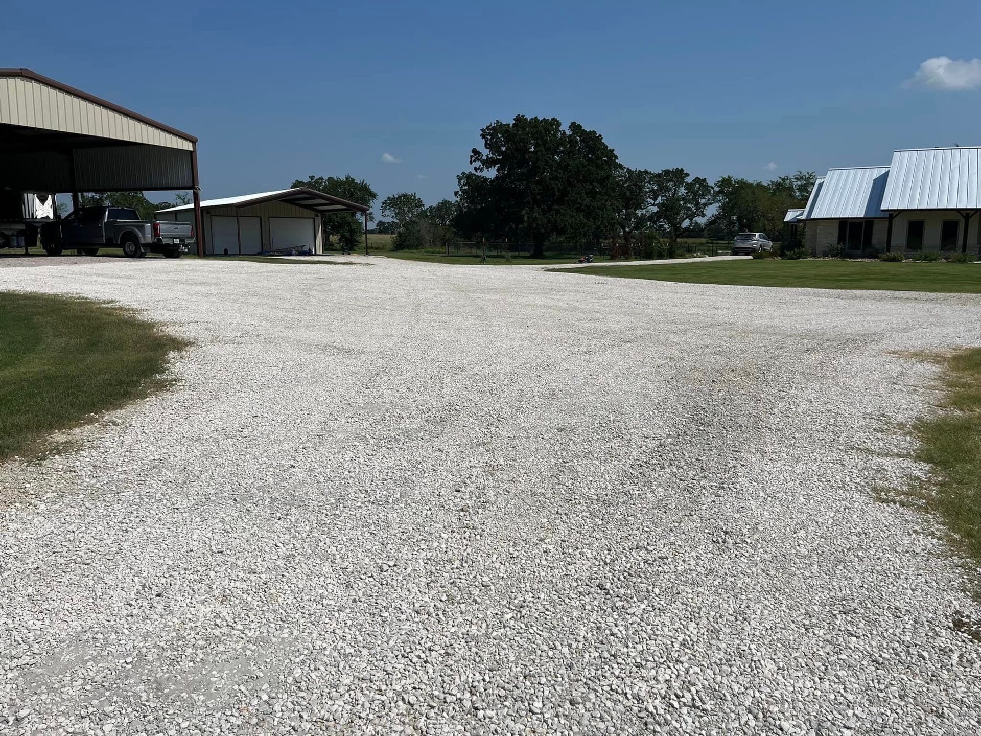 A gravel driveway leads past buildings and green grass under a blue sky.