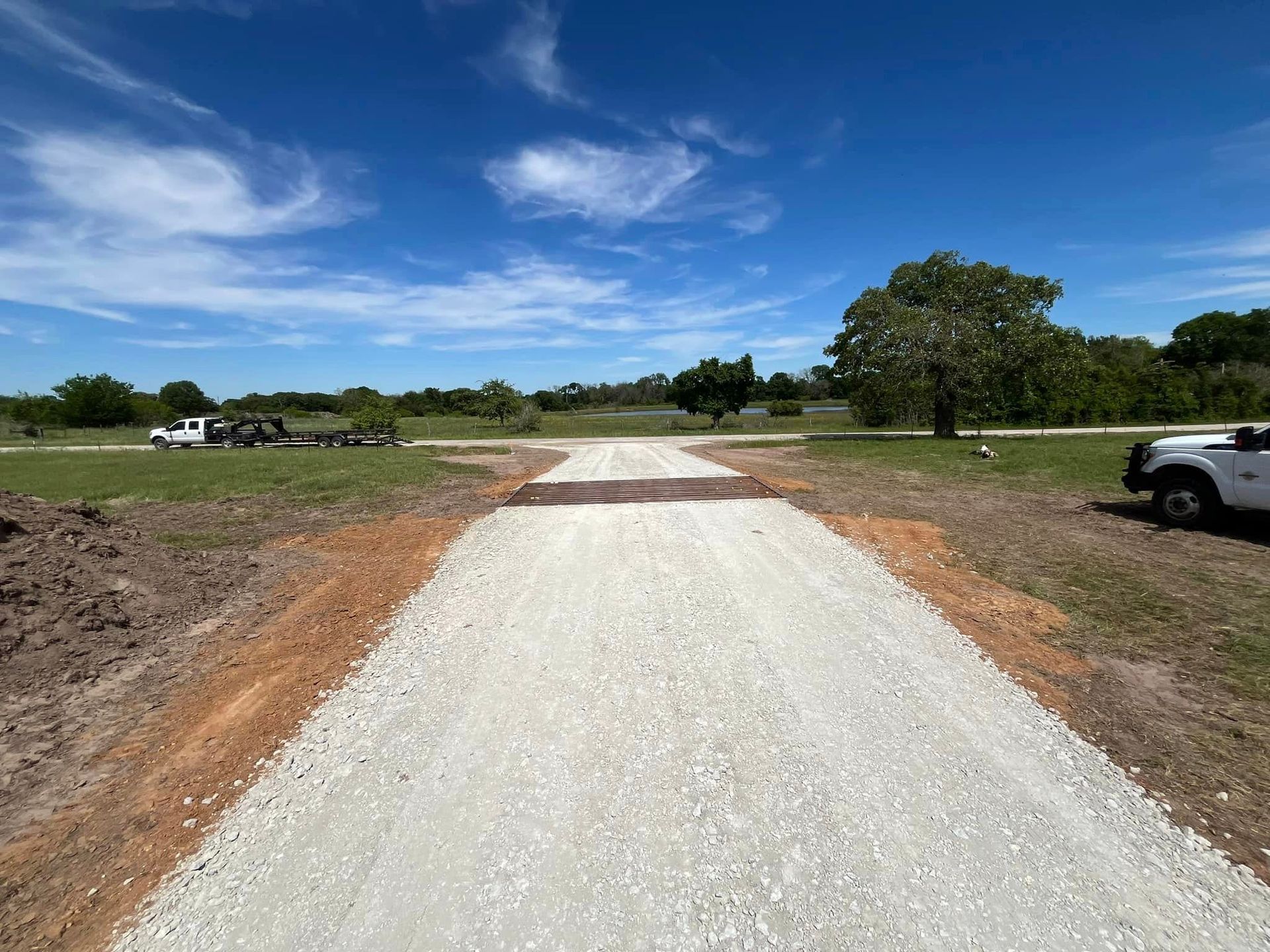 A gravel driveway splits towards a rural landscape under a bright blue sky.