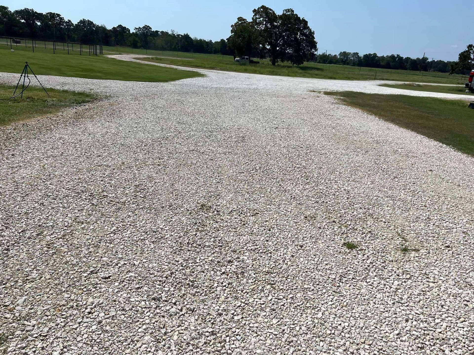 Gravel driveway intersecting with grass paths under a clear blue sky, a few trees are visible in the background.