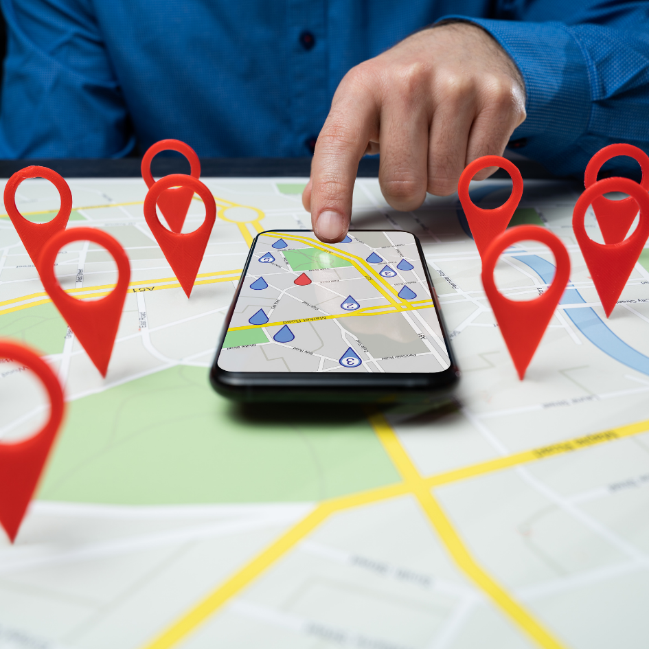 Person using phone with map app, surrounded by red location markers on a printed map.