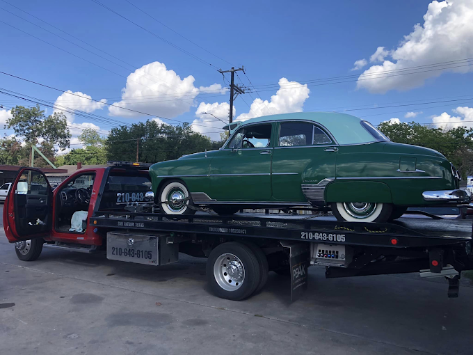 A green car is being towed by a tow truck.