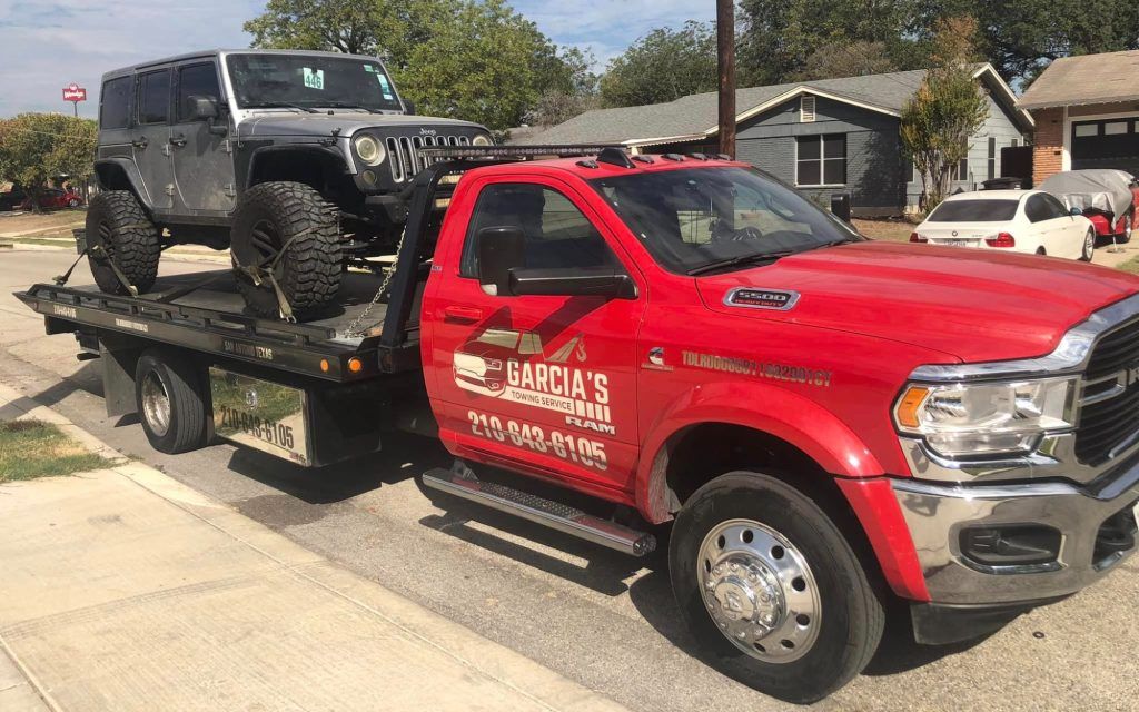A red tow truck is carrying a jeep on the back of it.