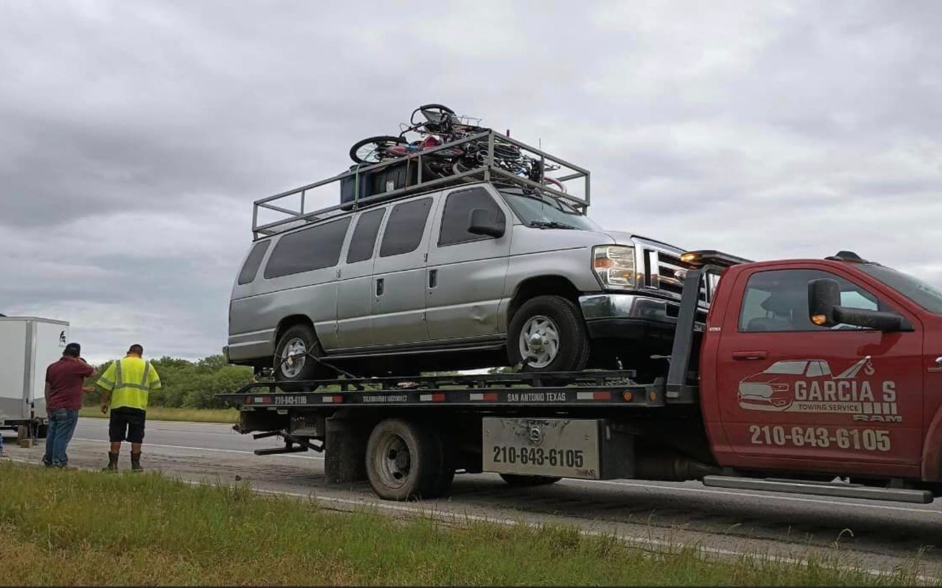 A tow truck is carrying a van with motorcycles on top of it.