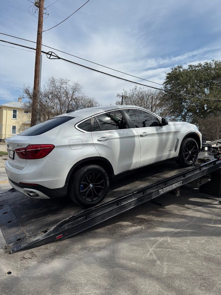 A white bmw x6 is being towed by a tow truck.