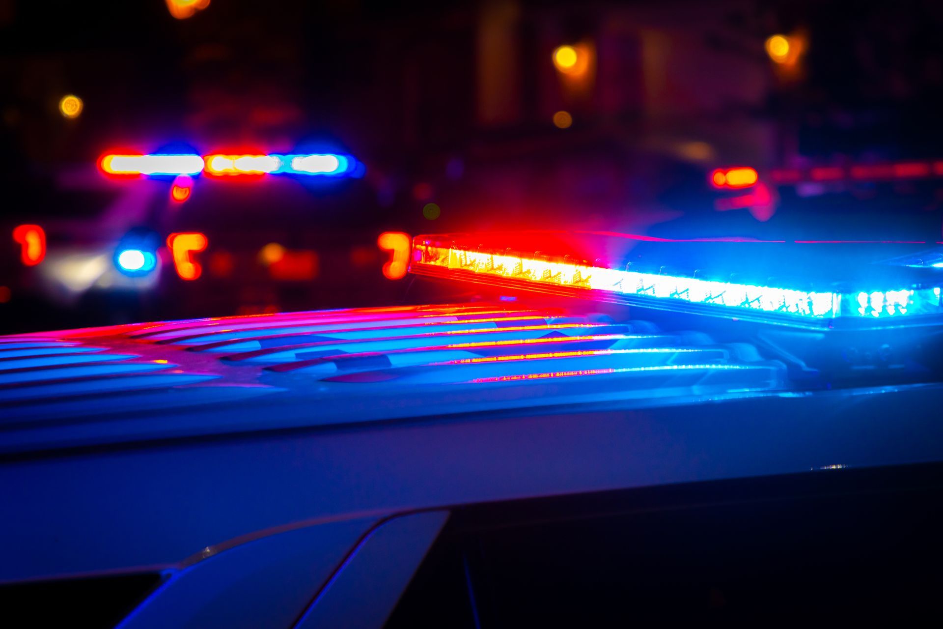 Police car light bar glowing red and blue at night, depicting an arrest scene