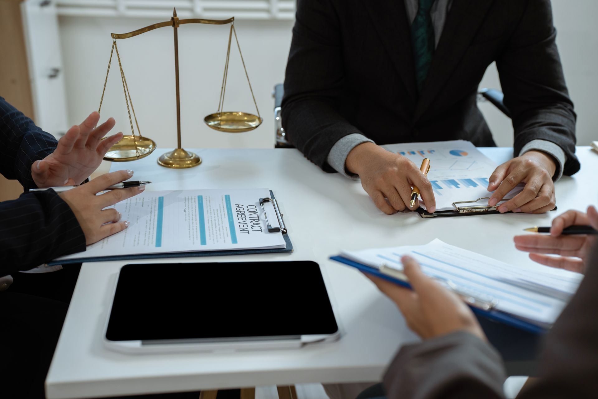 People at a table review documents, scales of justice in the background People at a table review documents, scales of justice in the background