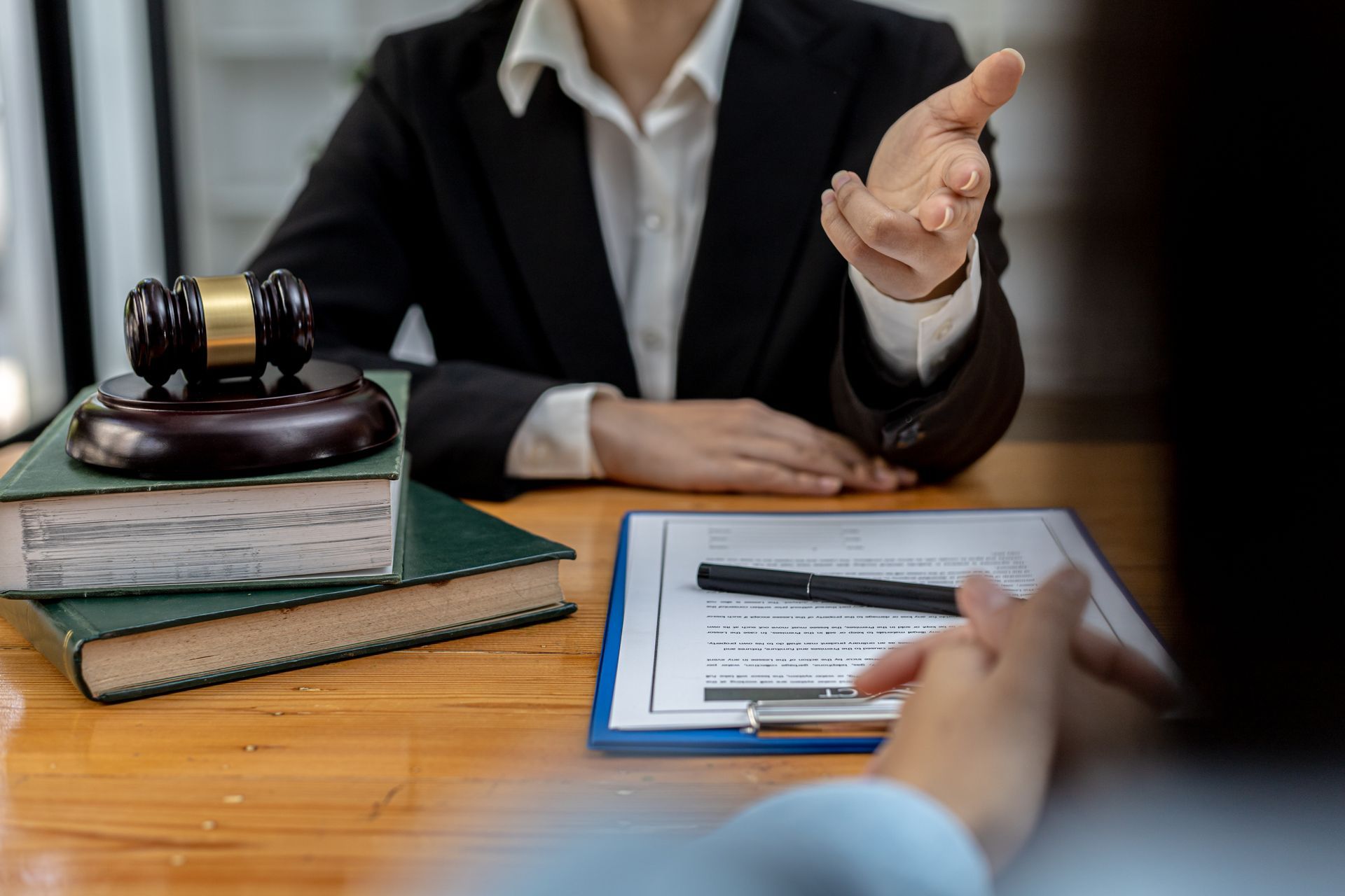 Attorney speaking to a client at a desk, gavel and law books present Attorney speaking to a client at a desk, gavel and law books present