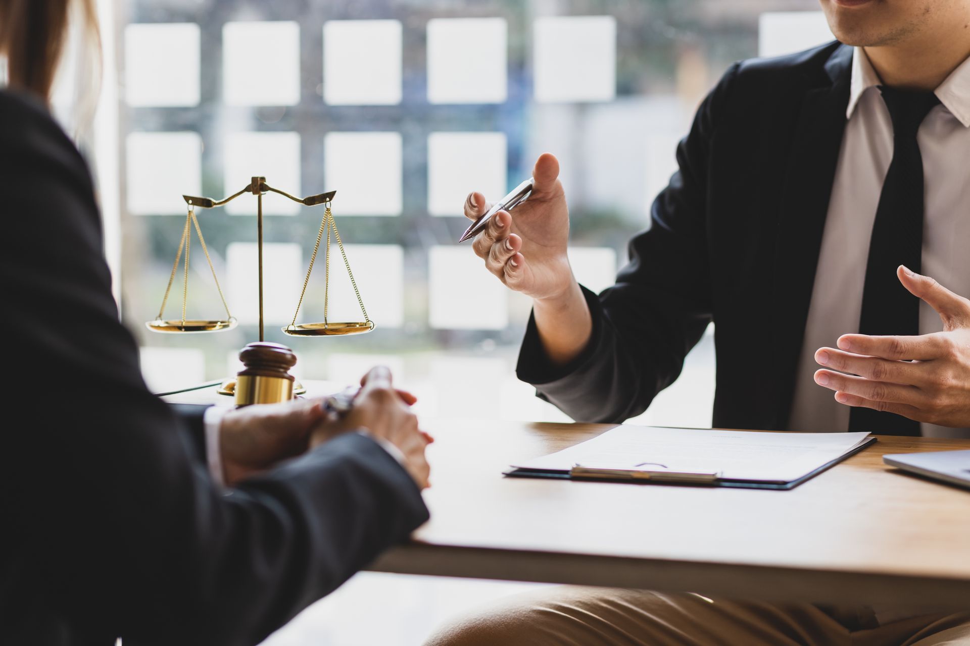Two people in suits at a table, one points at a clipboard