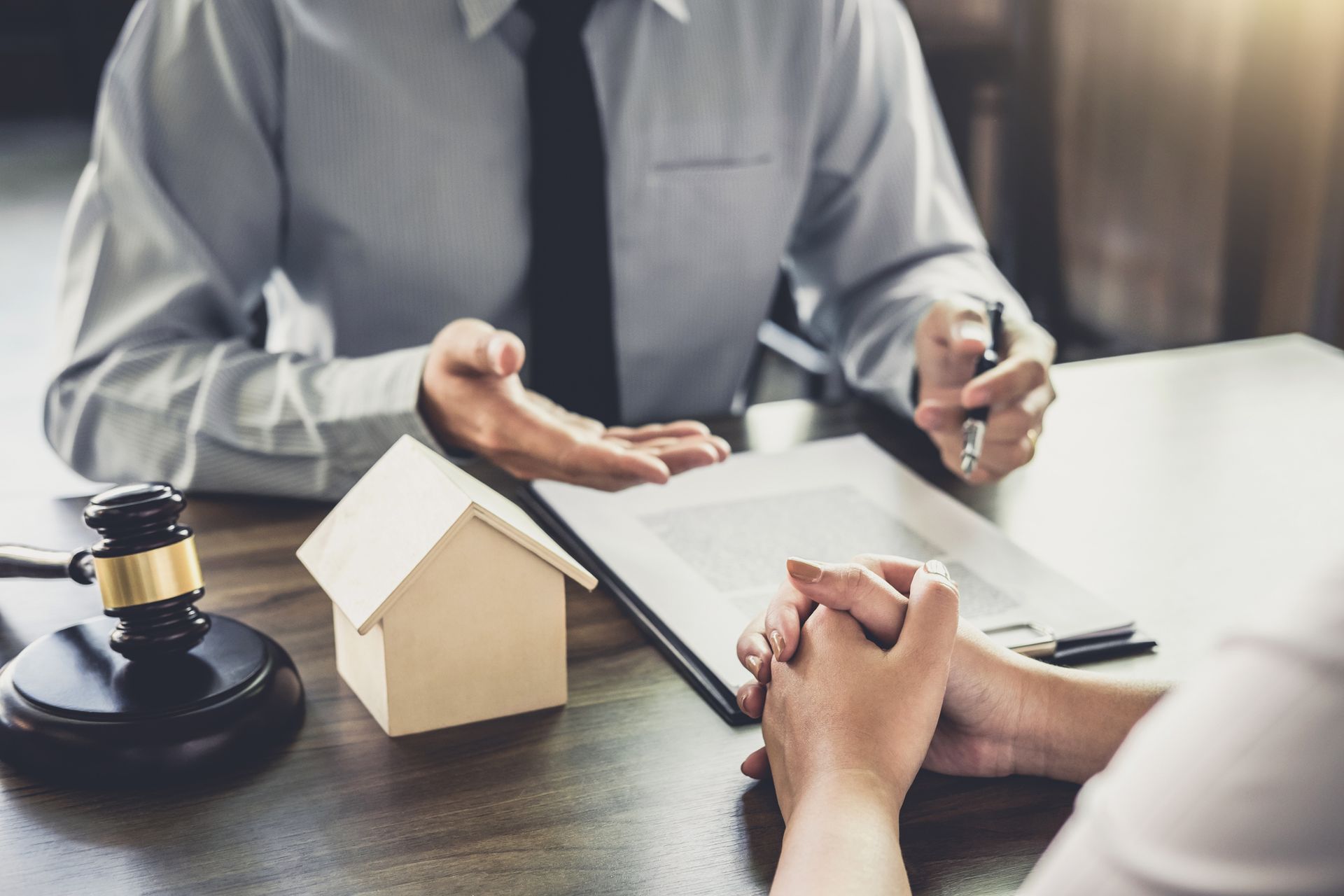 Attorney presenting documents to a client, with a gavel and house model on a table Attorney presenting documents to a client, with a gavel and house model on a table