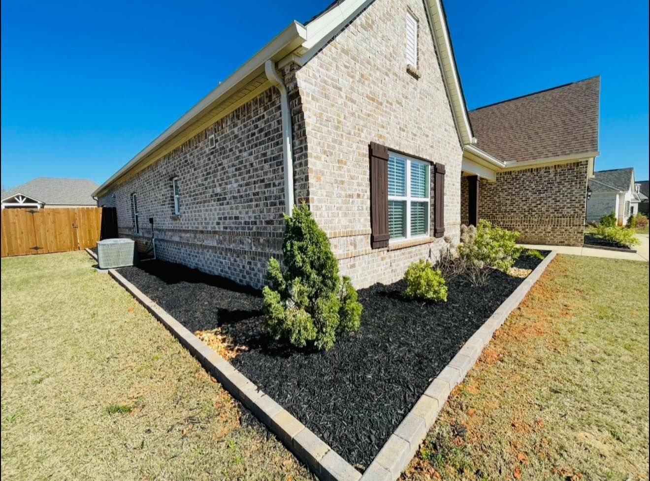 Tan brick house with black mulch landscaping under a bright blue sky.