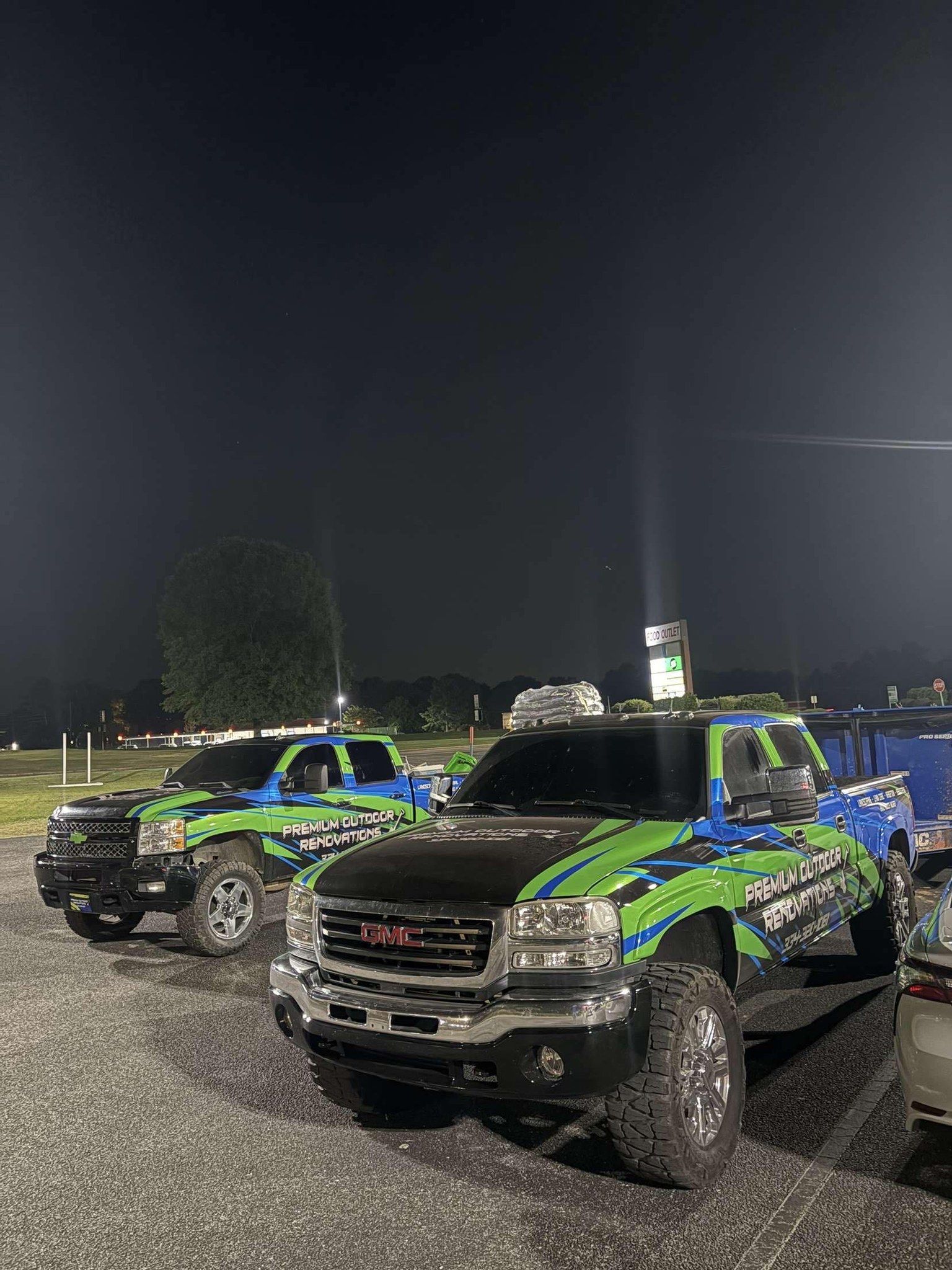 Two GMC trucks with blue and green graphics parked outdoors at night.