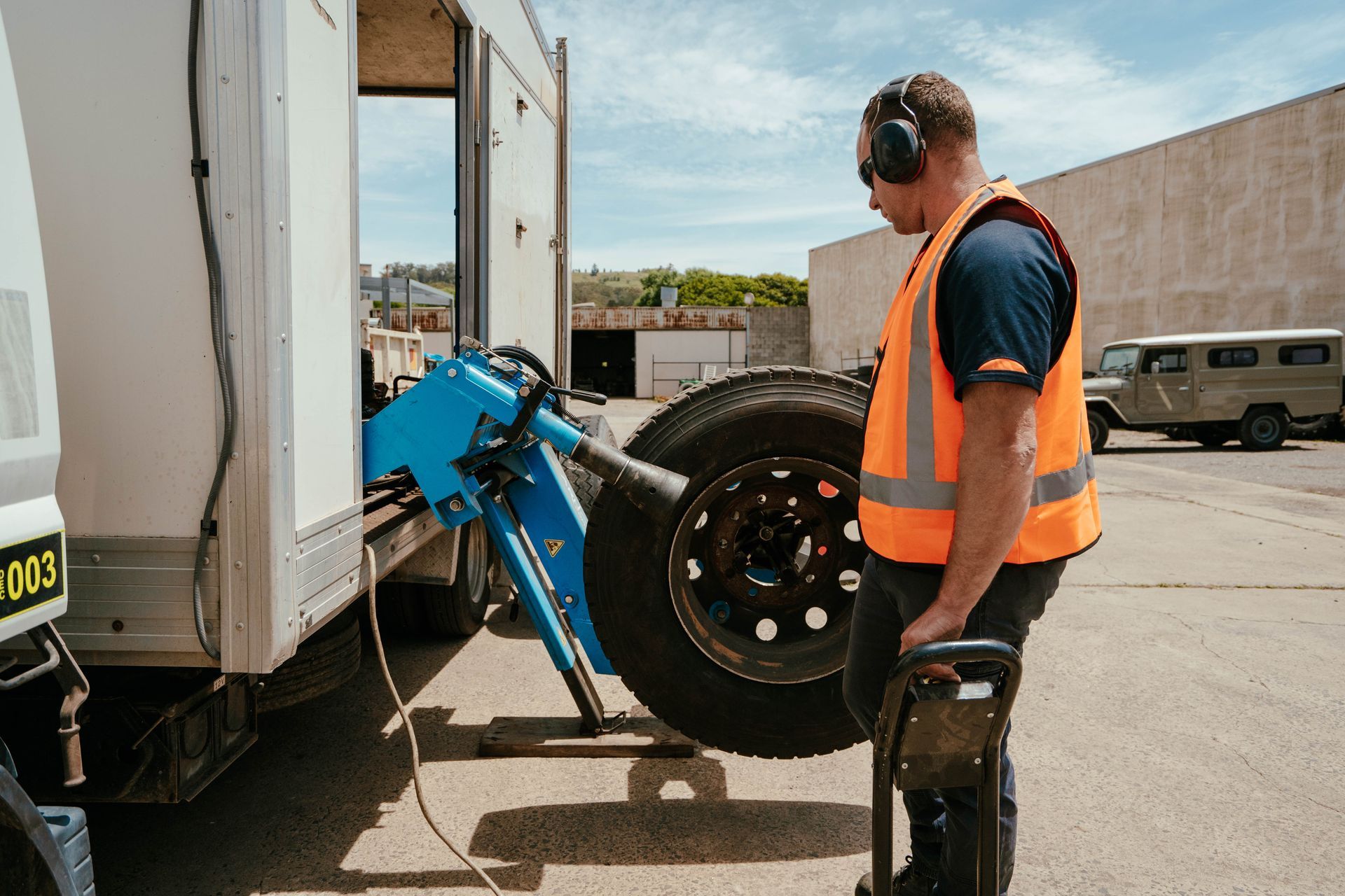 Worker In Orange Vest Loading a Truck Tyre — BOEX Tyres And Performance in Bowral, NSW
