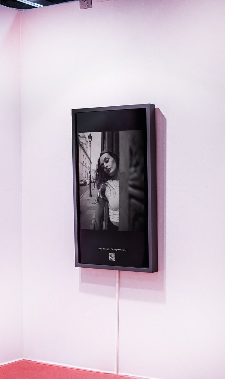 Black wall-mounted display showing a black-and-white portrait in a pink-lit room