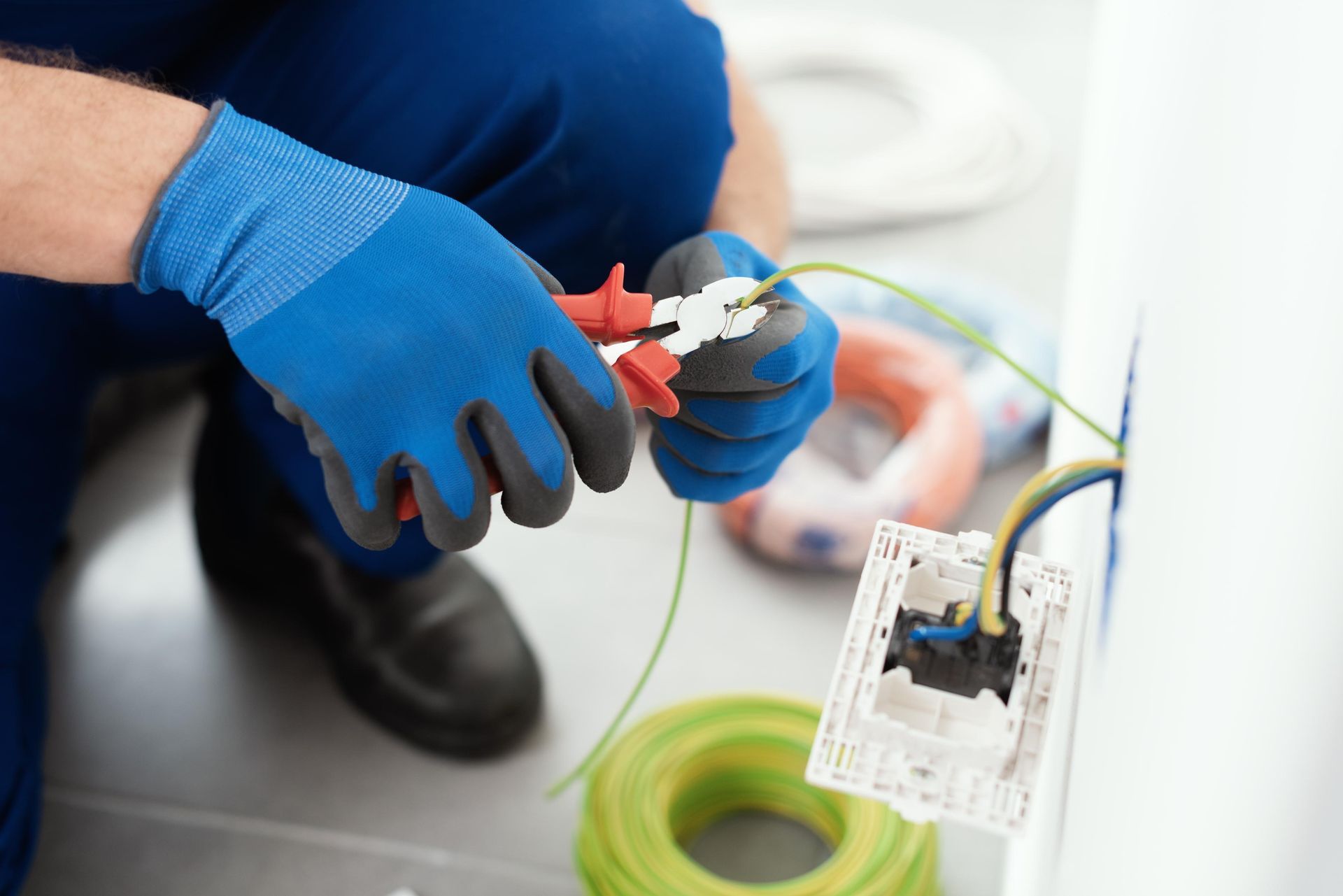 Electrician installing electrical outlet, cutting wire with pliers, wearing blue gloves.