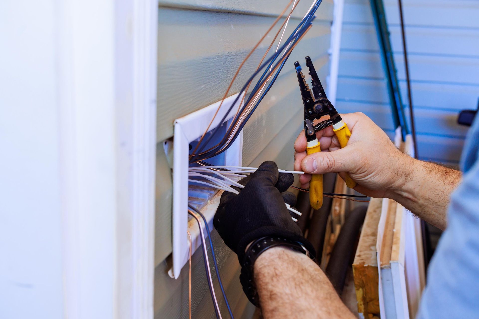 Person wearing gloves, stripping wires with pliers near an electrical panel.