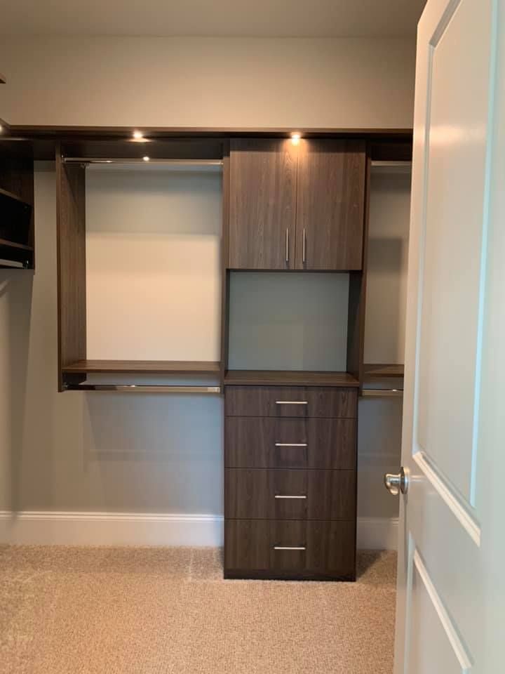 A modern closet interior features dark wood cabinetry, including a four-drawer dresser, upper storage, and hanging rods.