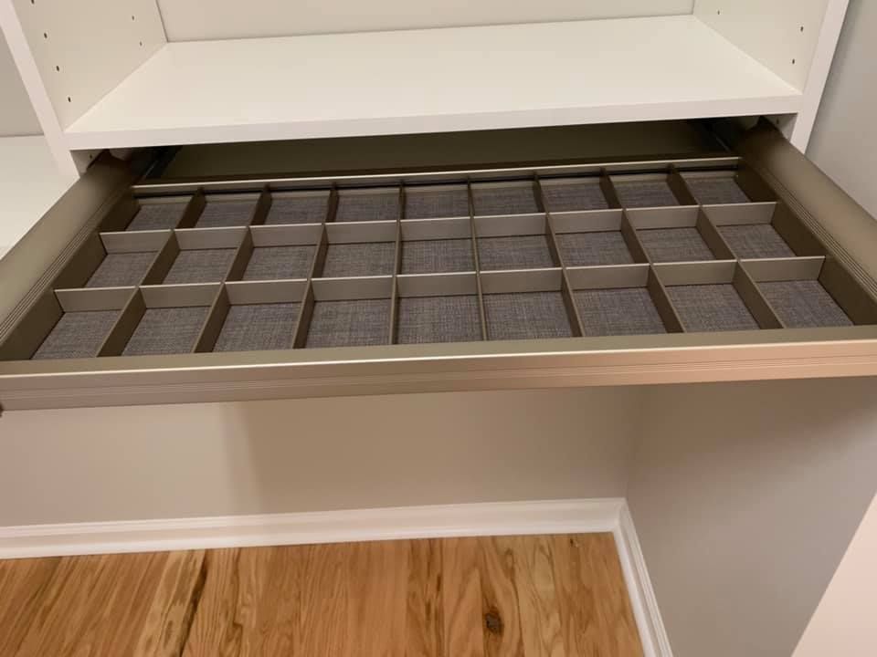 A pull-out jewelry organizer drawer with multiple fabric-lined grid compartments installed in a white closet cabinet.