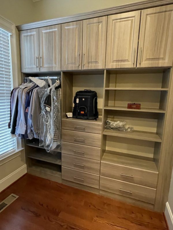 Custom light-wood closet shelving unit with hanging space, open shelves, and six drawers on a hardwood floor.