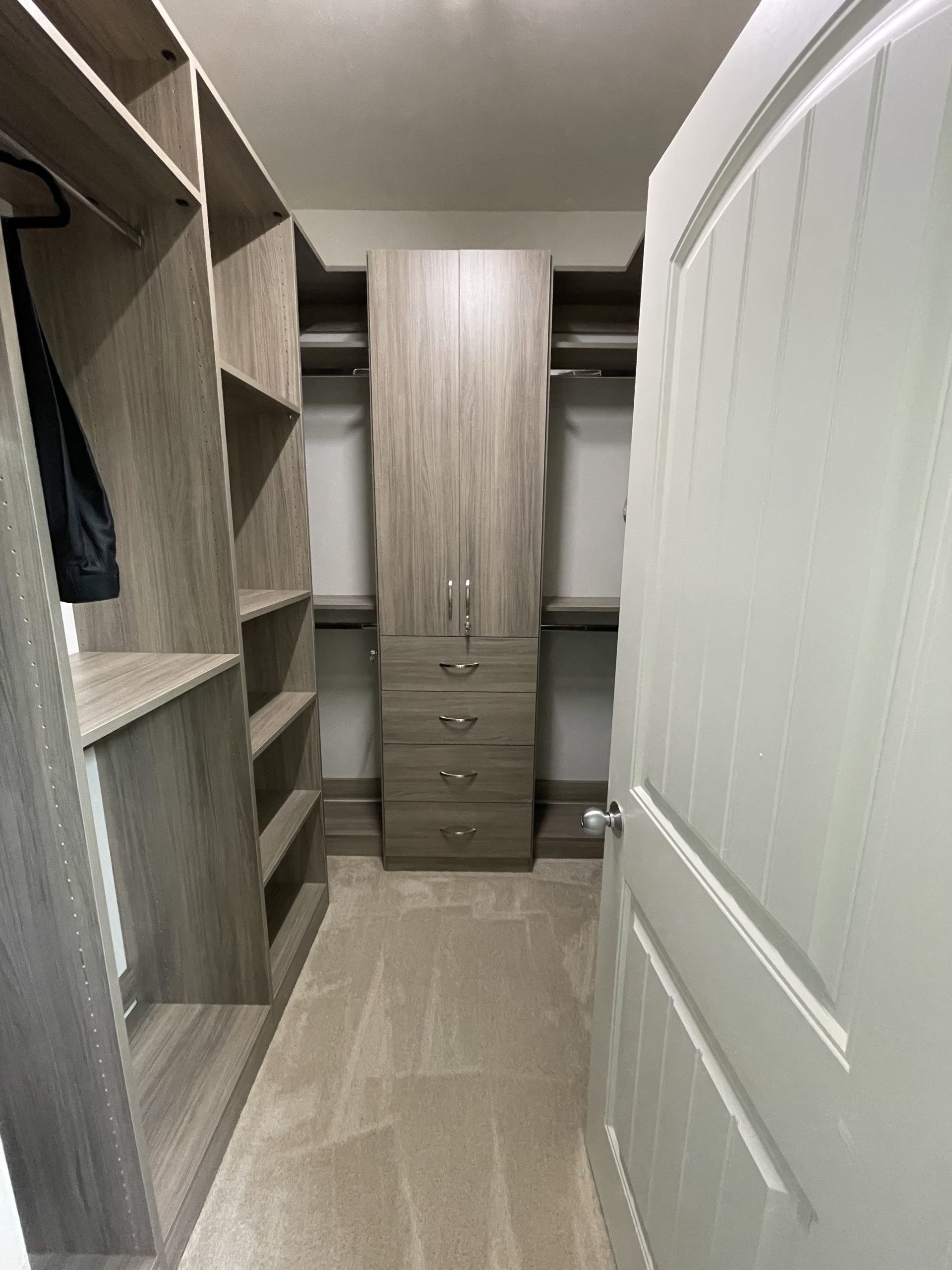 A walk-in closet featuring light brown wood shelving units, a center drawer cabinet, and a partially open white door.