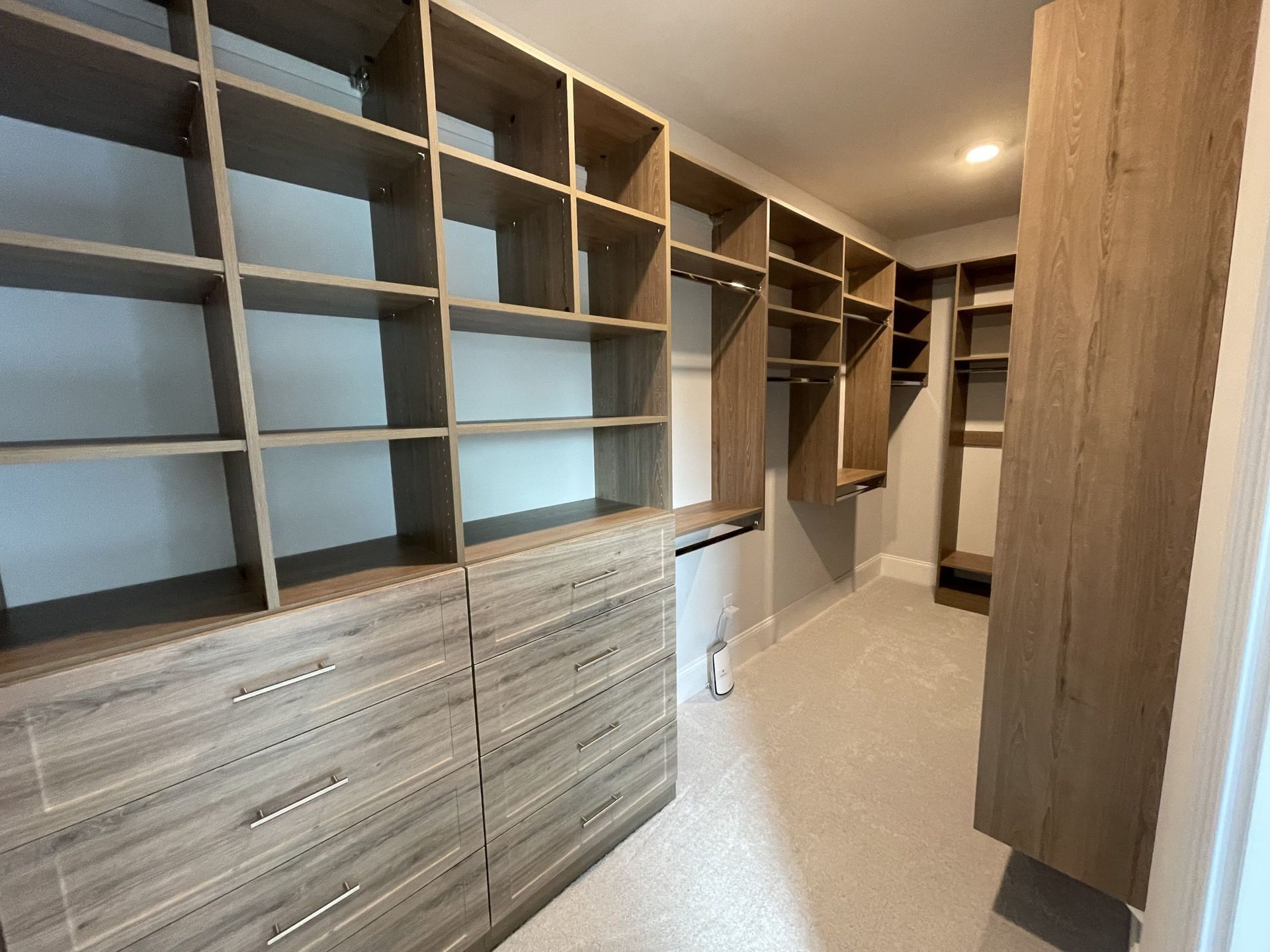 A walk-in closet featuring light wood-toned built-in shelving, drawers, and hanging rods with neutral carpet flooring.