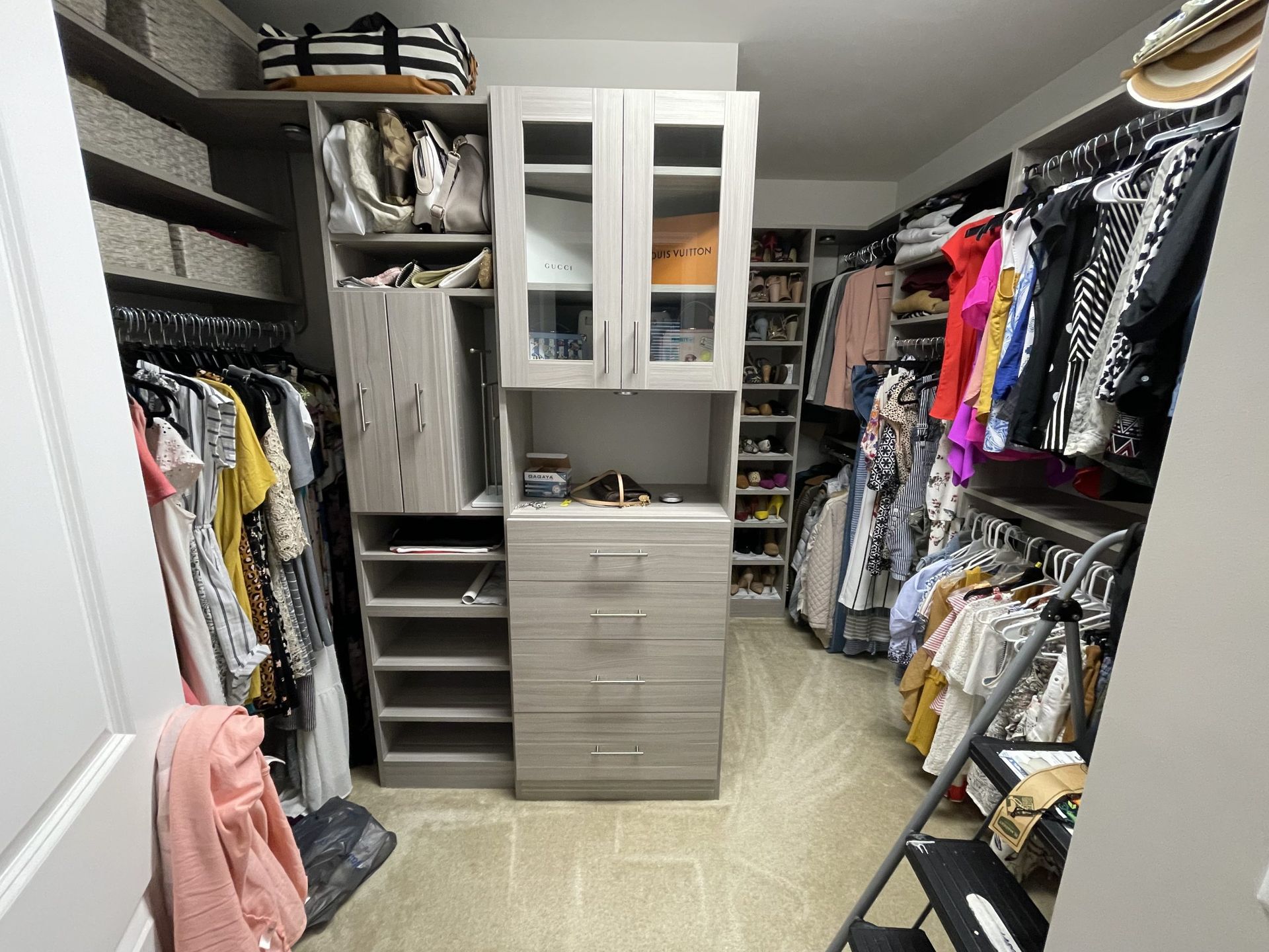 A walk-in closet featuring light wood cabinetry, shelving, hanging clothes, and a built-in dresser.