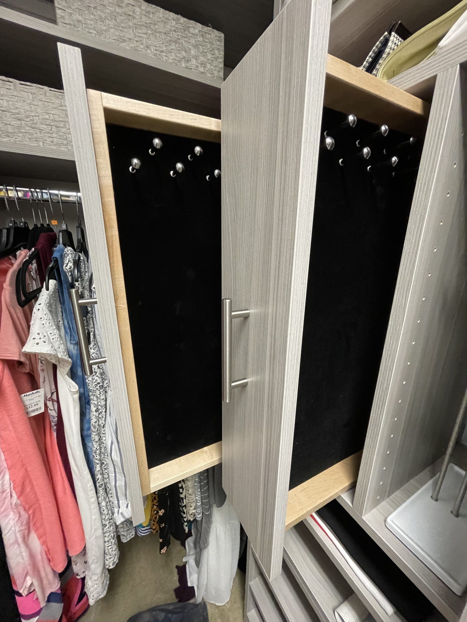 A pull-out jewelry rack with silver hooks on a black velvet display board, mounted inside a light-wood closet organizer.