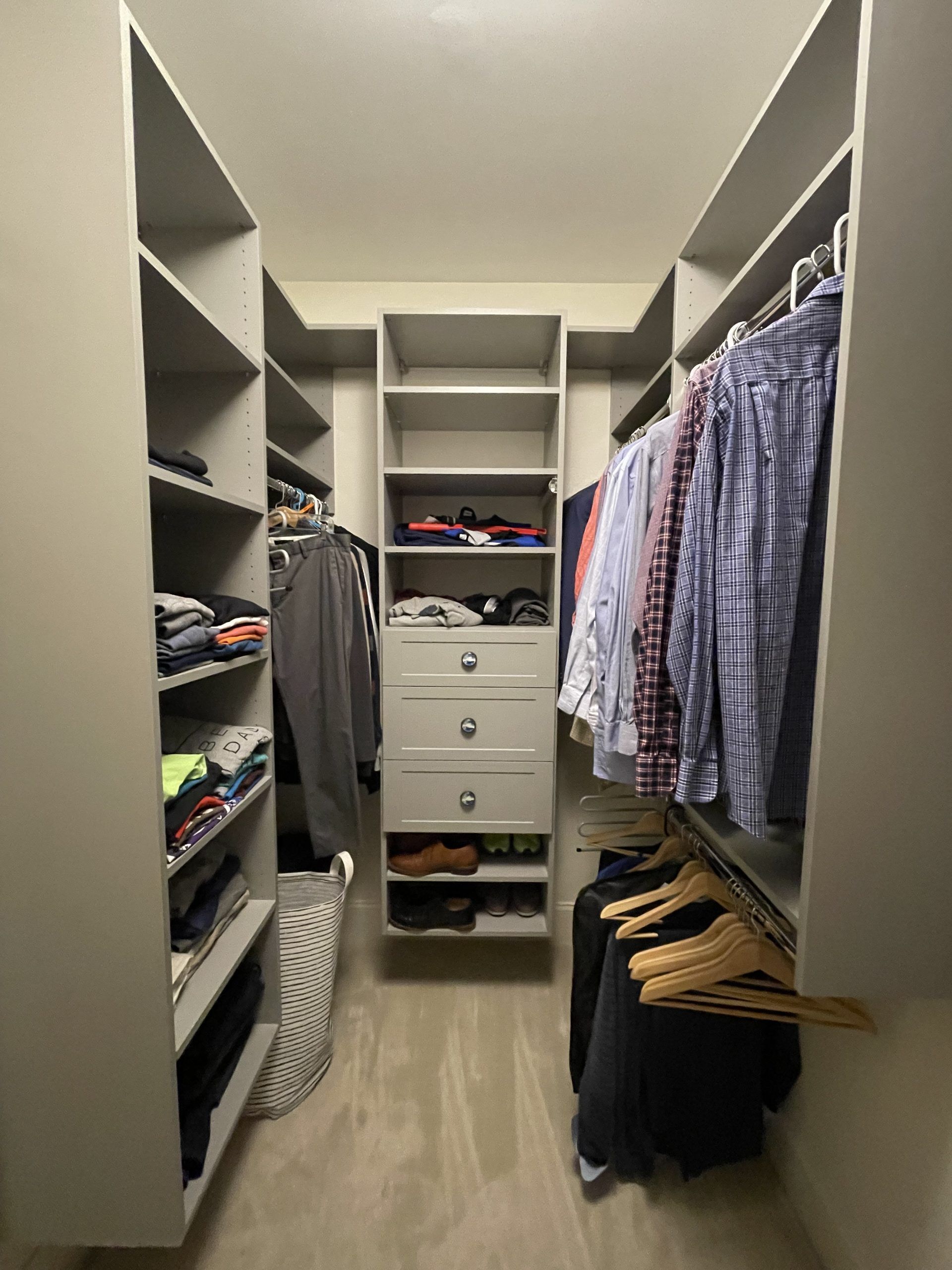 A walk-in closet with shelves and drawers in the center, and hanging clothes on both sides.