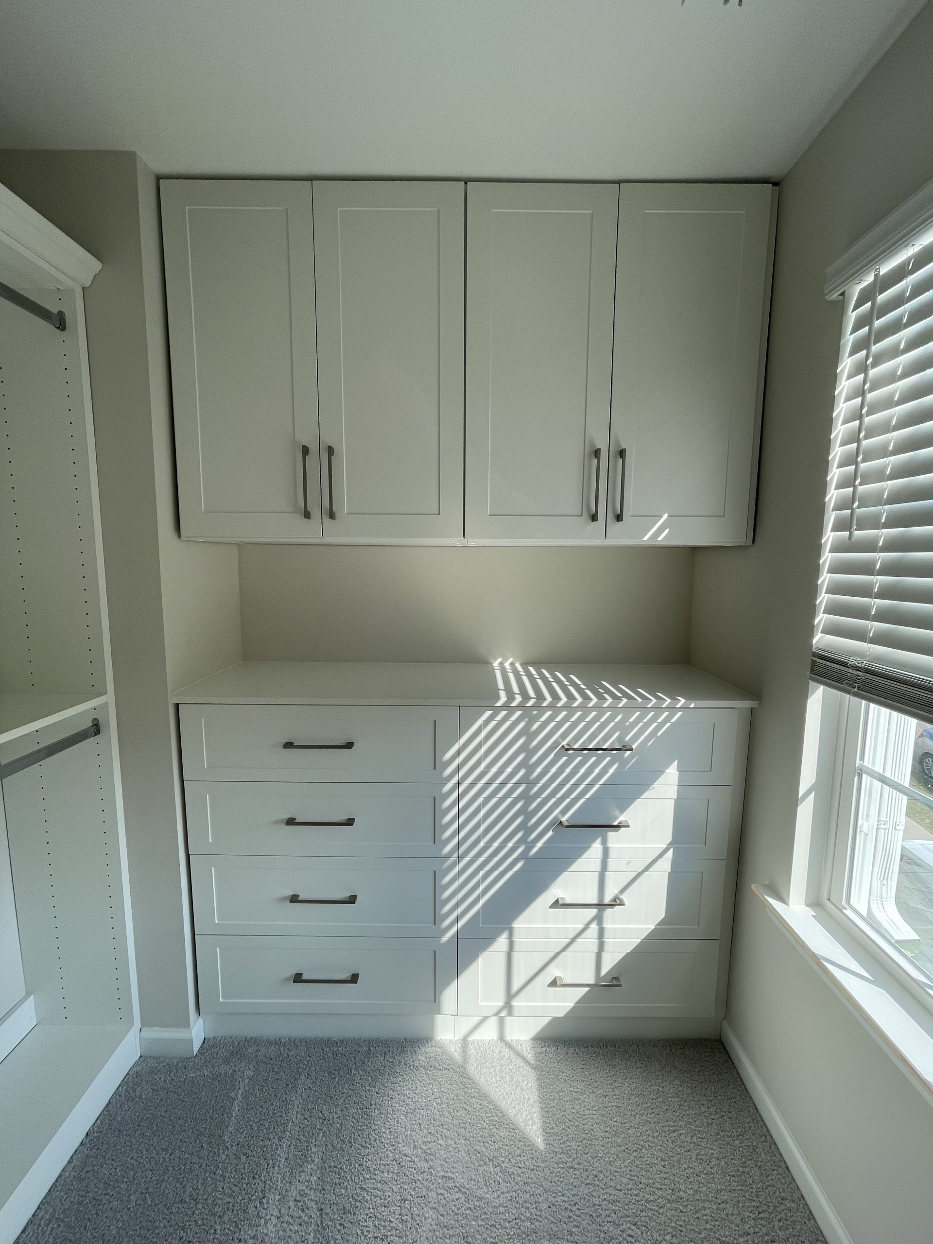 White built-in closet cabinetry featuring a four-drawer dresser beneath two upper cabinet doors, set in a carpeted room.