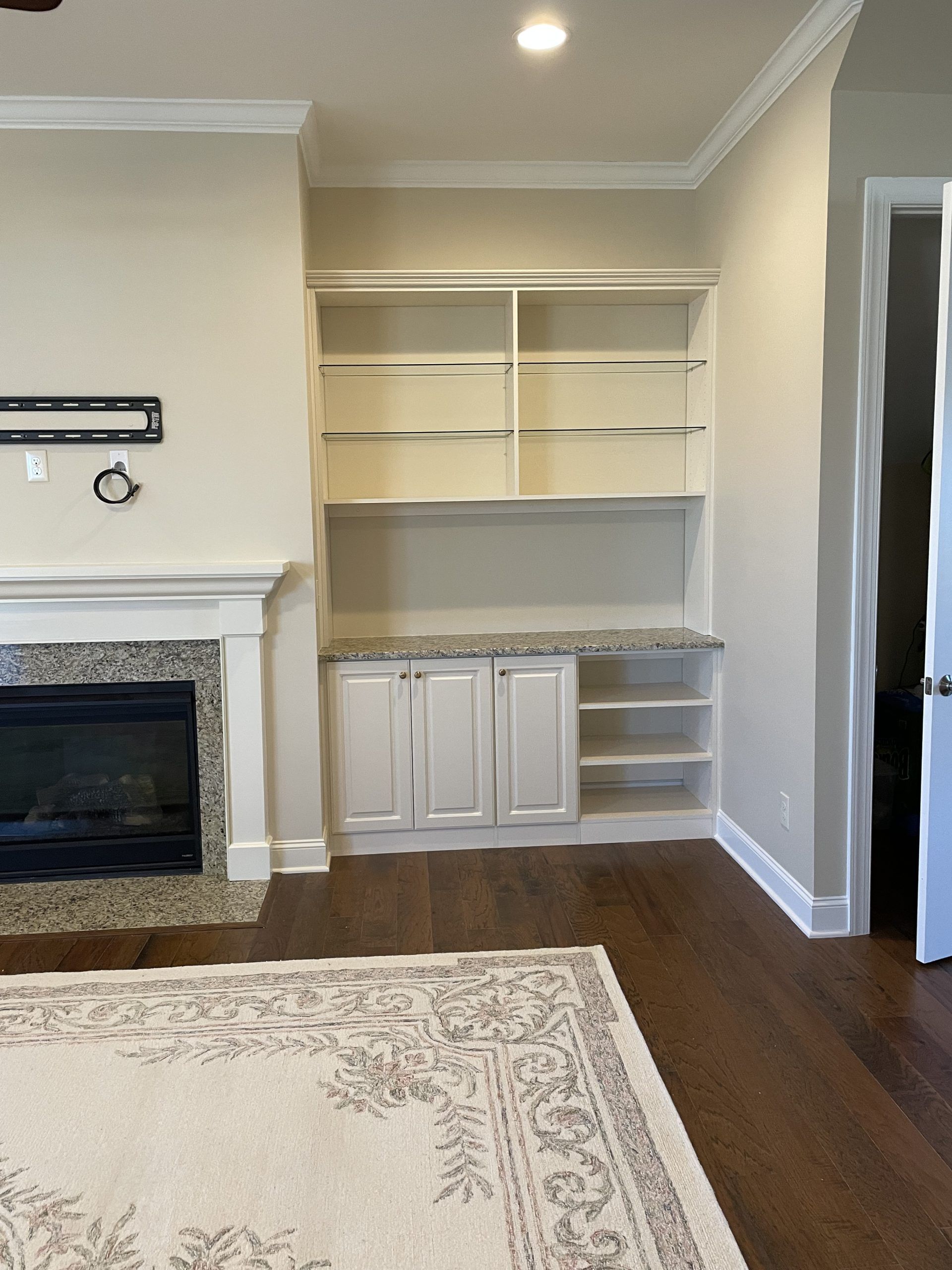 A light-colored fireplace next to built-in white cabinets with open shelving and a light stone countertop in a living room.