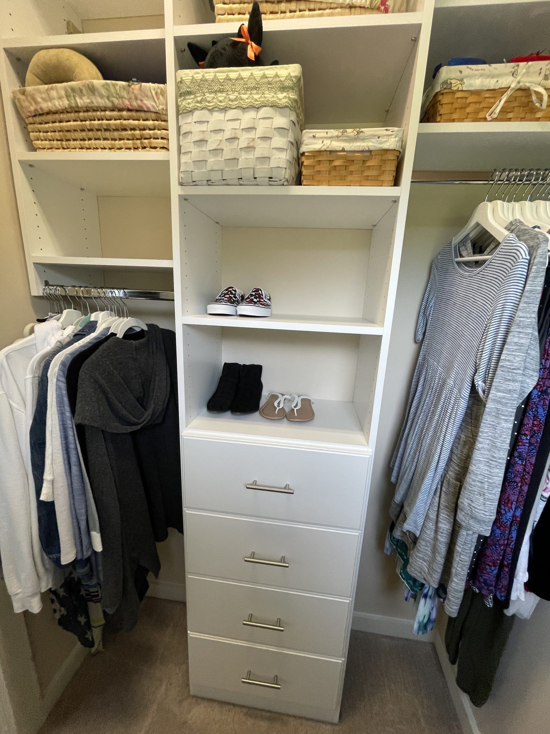 A white closet organizer featuring shelves, a four-drawer unit, and hanging clothing racks on both sides.
