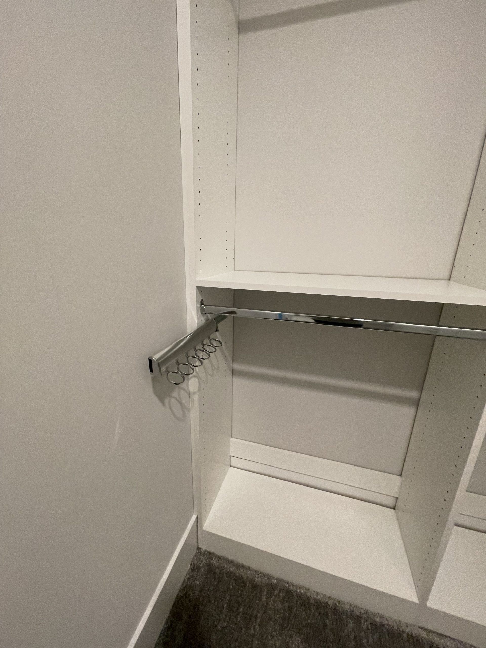 A white closet interior featuring a horizontal chrome clothes rod and a small pull-out chrome valet rod on the left wall.