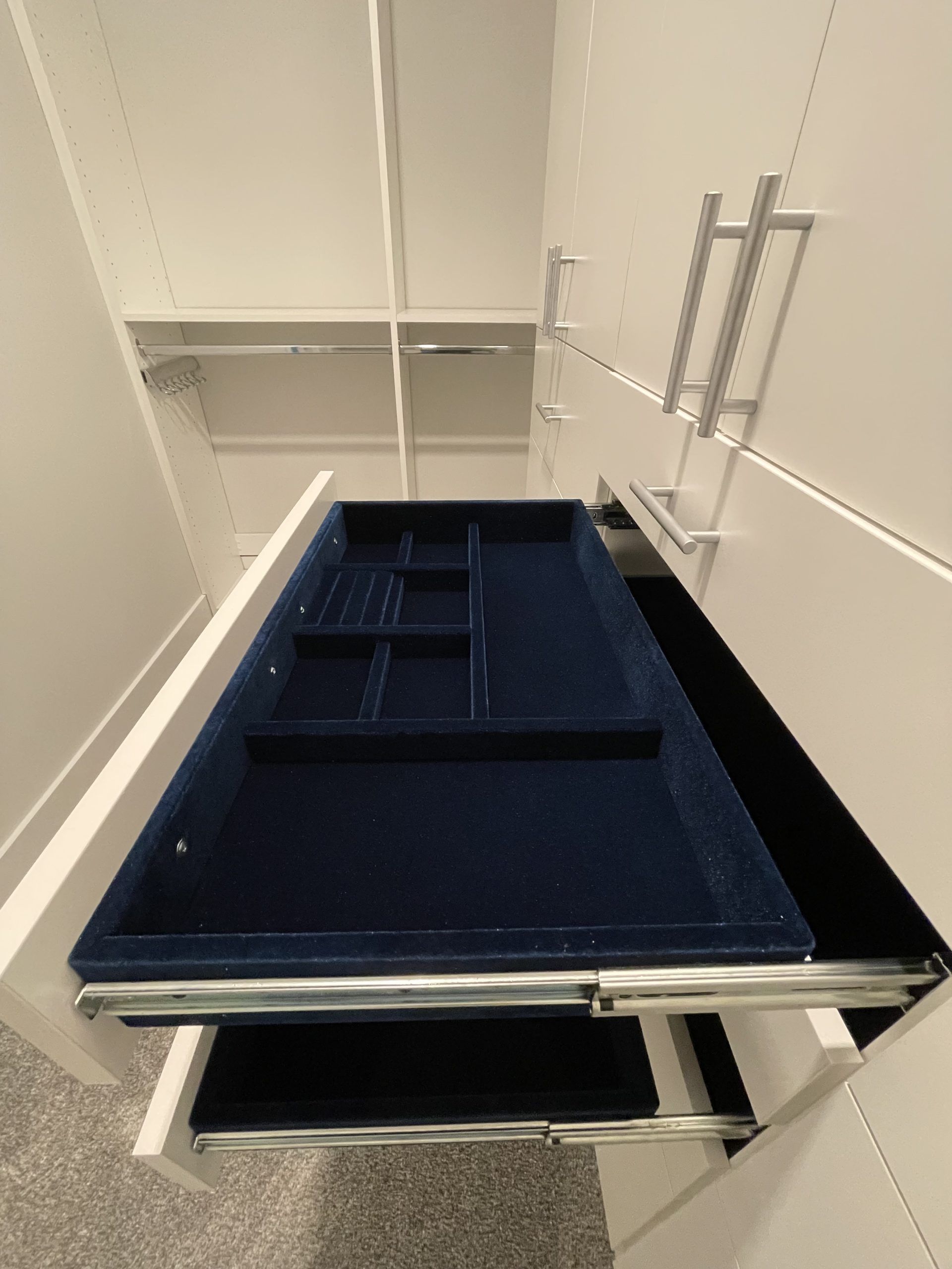 Two open white closet drawers with blue velvet jewelry organizer inserts, viewed from above in a walk-in closet.