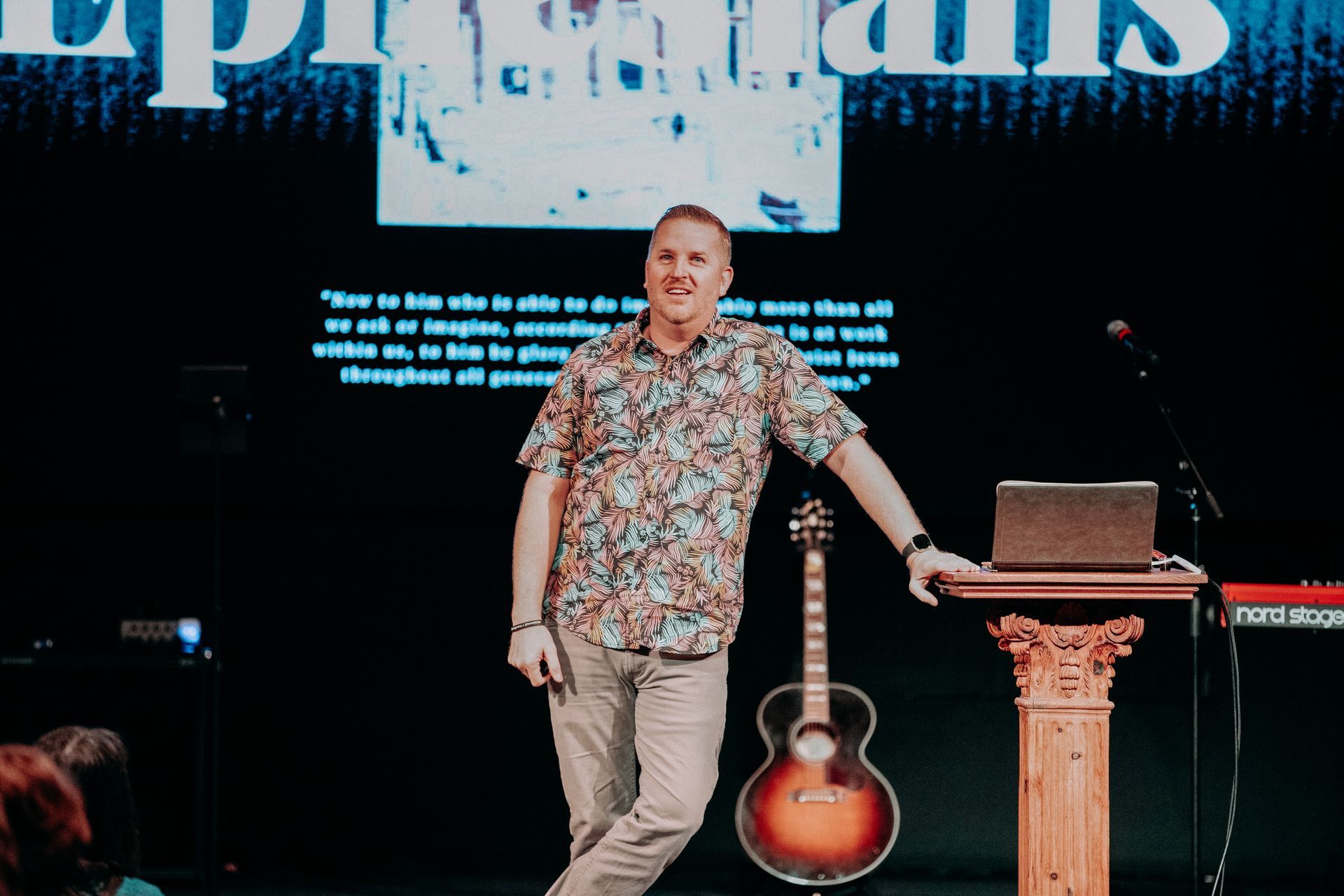 A man is standing on a stage with a guitar and a laptop.
