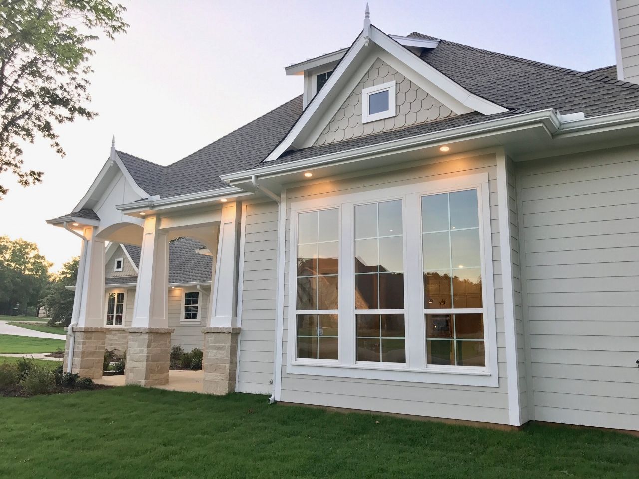 Light gray house with white trim, bay window, and gabled roof, set on green grass.