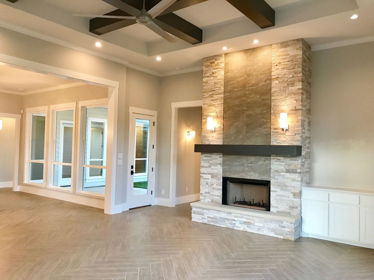 Living room with a stone fireplace, light wood floor, and large windows.
