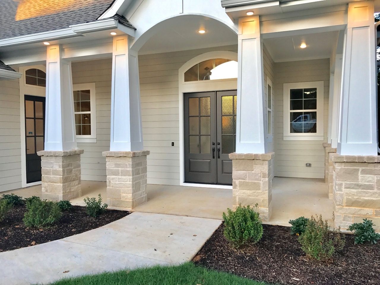 A house with a front porch, stone columns, double doors, and a walkway.