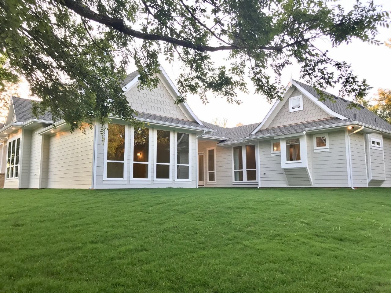 Beige house with large windows, set in a grassy yard under a tree.