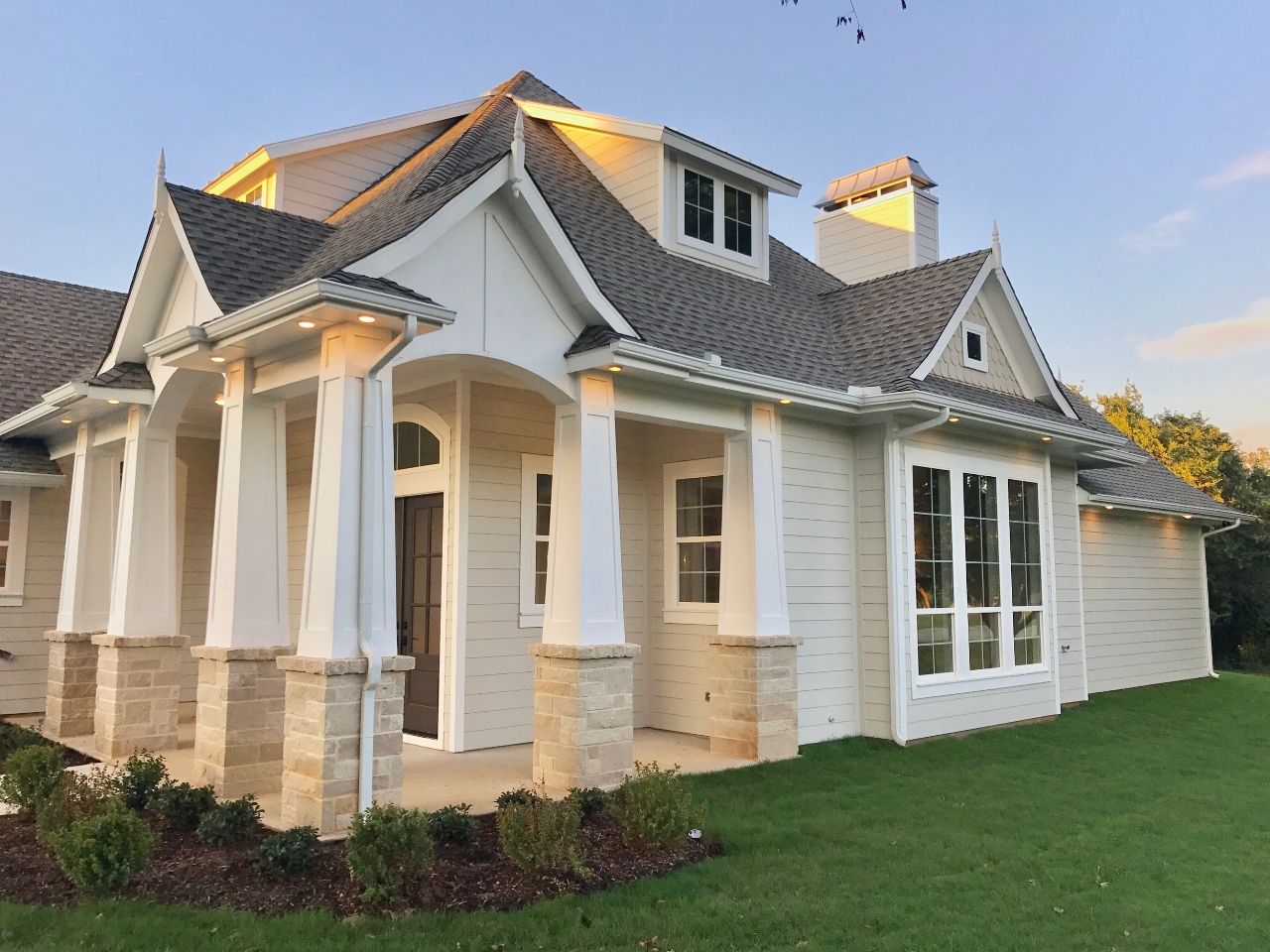 White brick house with columns, a grey roof, and green lawn.