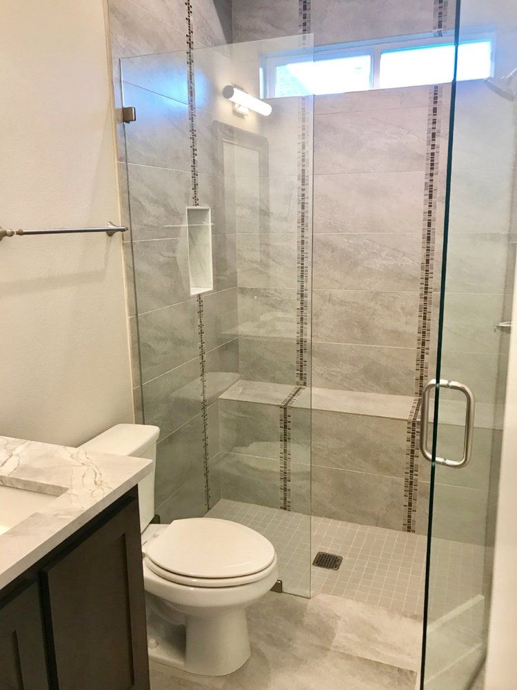 Bathroom with glass shower, toilet, and vanity. Gray tile and brown cabinet.