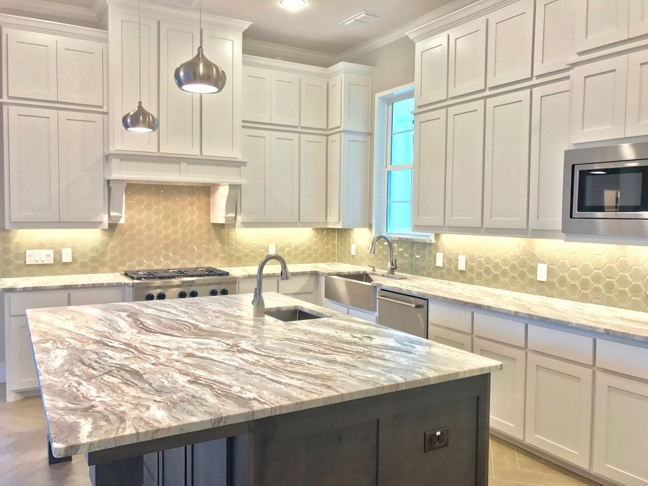 Modern kitchen with white cabinets, marble island, stainless steel appliances, and gold backsplash.