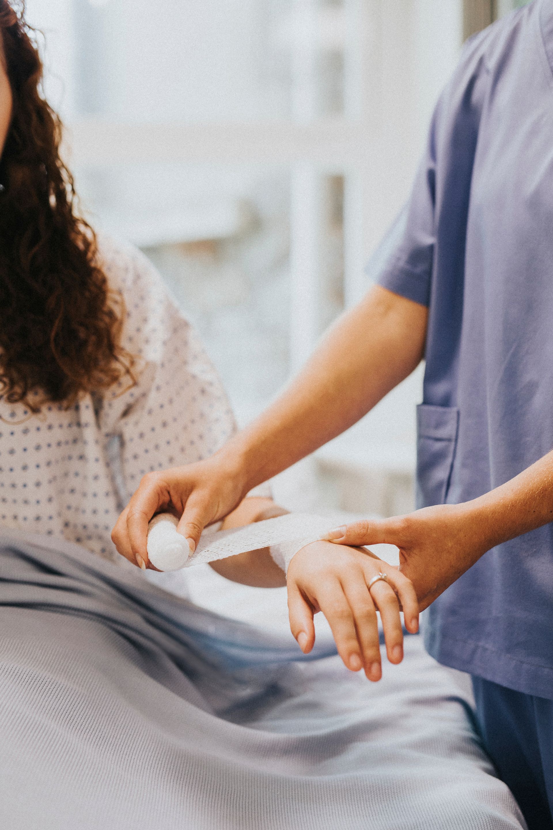 A medical professional wraps a patient's wrist with a white bandage in a clinical setting.