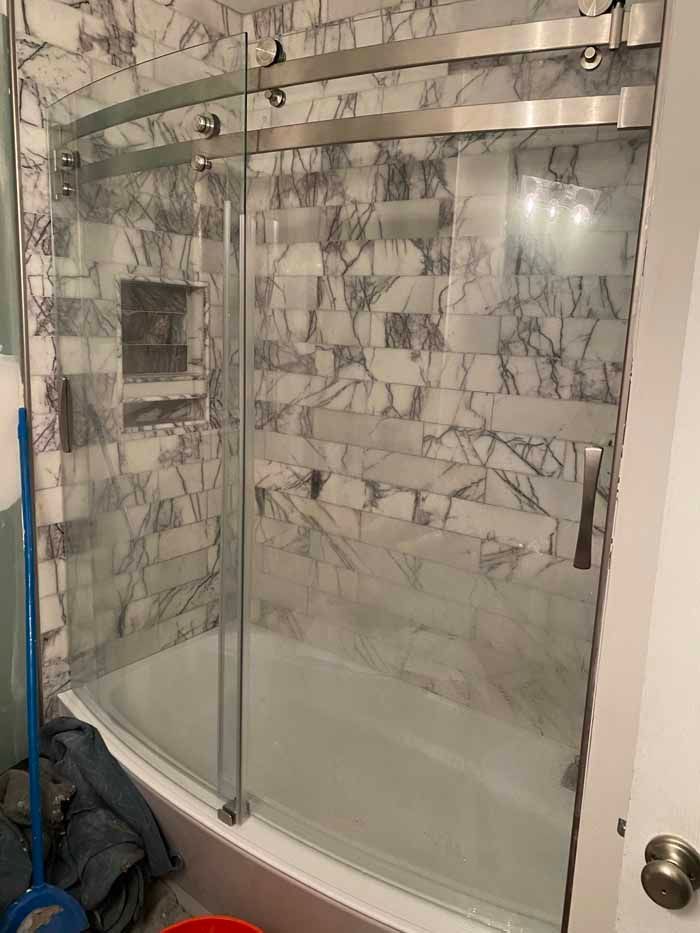 Corner shower with frosted glass sliding doors and gray marble-patterned tile walls